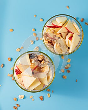 Proper nutrition, breakfast. Welness - granola with yogurt and fruits: banana and apple, in glass cups on a blue background. Top