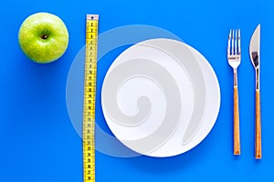 Proper nutrition with dietary fibre for weight loss. Apple on plate near measuring tape on blue background top view