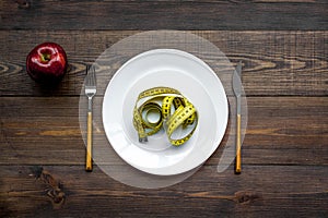 Proper nutrition for lose weight. Empty plate, apple and measuring tape on dark wooden background top view