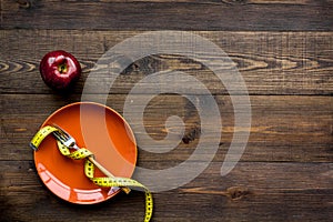 Proper nutrition for lose weight. Empty plate, apple and measuring tape on dark wooden background top view copy space