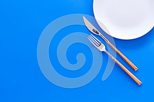 Proper nutrition for slimming. Empty plate with fork and knife on blue background top view copy space