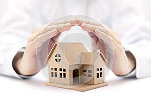 Property insurance. House miniature covered by hands.