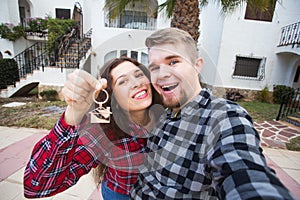 Property, real estate and rent concept - Happy funny young couple showing a keys of their new house