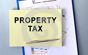 PROPERTY TAX text written on notepad with pencil. Notepad on a folder with diagrams.