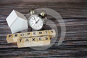 Property Taxes alphabet letter with house model and alarm clock on wooden background