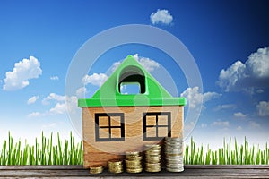 Property value growth concept with wooden house and scale of money against natural background