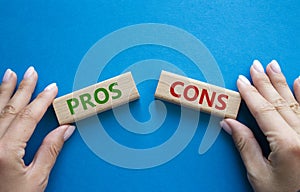 Pros vs Cons symbol. Concept word Pros vs Cons on wooden blocks. Businessman hand. Beautiful blue background. Business and Pros vs