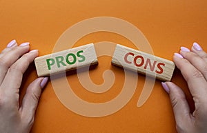 Pros vs Cons symbol. Concept word Pros vs Cons on wooden blocks. Businessman hand. Beautiful orange background. Business and Pros
