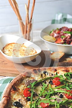 Prosciutto and arugula salad in a white bowl and cherry tomatoes pizza over wooden background. Red plaid tablecloth
