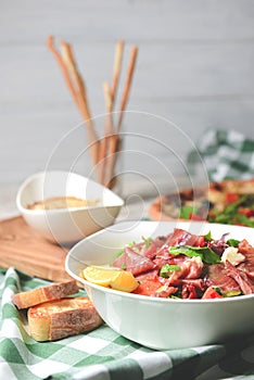 Prosciutto and arugula salad in a white bowl and lasagna over wooden background