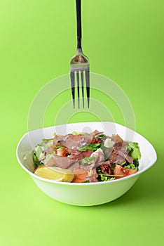 Prosciutto and arugula salad in a white bowl over bright green background. Italian cuisine concept
