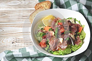 Prosciutto and arugula salad in a white bowl over wooden background. Green plaid tablecloth
