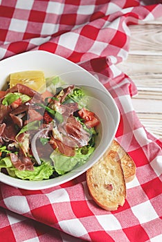 Prosciutto and arugula salad in a white bowl over wooden background. Red plaid tablecloth
