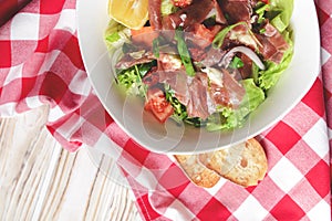 Prosciutto and arugula salad in a white bowl over wooden background. Red plaid tablecloth