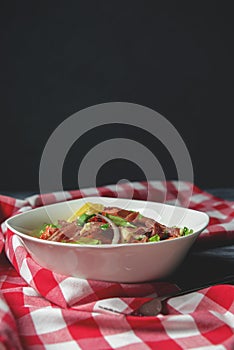 Prosciutto and arugula salad in a white bowl over wooden background. Red plaid tablecloth