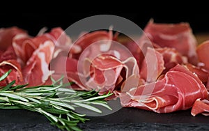 Prosciutto crudo or jamon meat with rosemary on serving board on black background. Sliced into thin pieces of ham puts on cutting