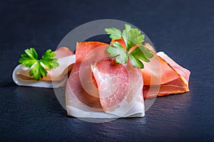 Prosciutto. Curled Slices of Delicious Prosciutto with parsley leaves on granite board. Prosciuto with spice cherry tomatoes photo