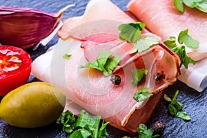 Prosciutto. Curled Slices of Delicious Prosciutto with parsley leaves on granite board. Prosciuto with spice cherry tomatoes photo