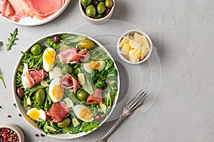 Prosciutto di Parma salad with olives, parmesan cheese, eggs and arugula on gray background. Italian appetizer. Top view