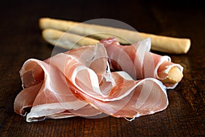 Prosciutto ham and grissini bread sticks. Isolated on dark wood.