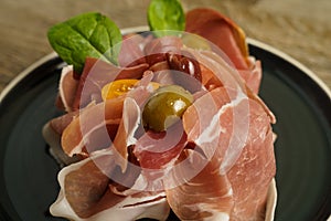 Prosciutto ham plate with olives on wooden table