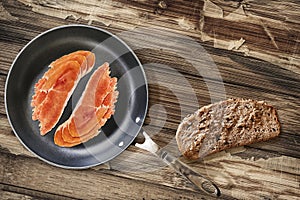 Prosciutto Rashers In Teflon Frying Pan And Slice Of Brown Bread Set On Old Cracked Flaky Wooden Garden Table photo