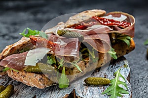 Prosciutto sandwich, Ciabatta with prosciutto, sun-dried tomatoes, gherkins, parmesan and arugula, Food recipe background. Close