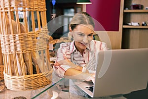 Prosperous owner of bakery using her laptop while contacting suppliers