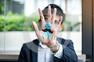 Prostate Cancer Awareness month, Business Man holding light Blue Ribbon with mustache for supporting people living and illness. Me