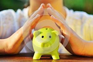 Protect your savings - with hands covering green piggy bank