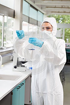 A protected scientist pouring liquid in a flask