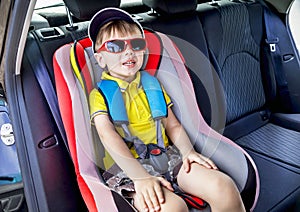 Protection in the car. Caucasian child is sitting and fastening with security belt in safety car seat.