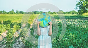 Protection and love of earth. Little girl holding planet in hands against green spring background. Earth day holiday concept.