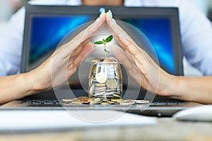 Protection of money from online transaction concept, with womanâ€™s hands covering a jar of coins above a notebook