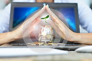 Protection of money from online transaction concept, with womanâ€™s hands covering a jar of coins above a notebook