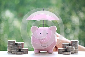 Protection,Piggy bank with hand holding the umbrella on natural green background, Finance insurance and Safe investment concept