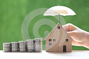 Protection  Stack of coins money and Model house with hand holding the umbrella on natural green background  Finance insurance and