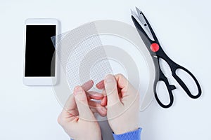 Protective film for the smartphone screen in the hands of caucasian woman. Scissors and phone. White background