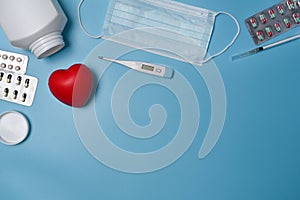 Protective mask, red heart, thermometer and medicine pills on blue background.