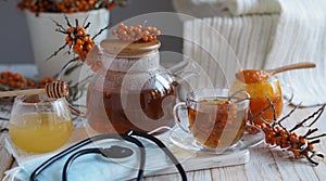 Protective medical mask with a phonendoscope and sea buckthorn branches with berries, tea, honey and a warm scarf on a white