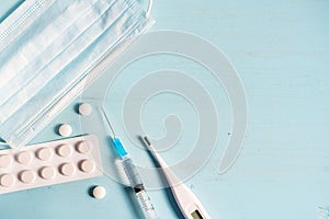 Protective medical mask, syringe, thermometer, tablets on a blue wooden background. Copy space