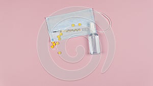 Protective medicine mask, antiseptic thermometer and pills on pink background, flat lay. Concept of doctor table and health care