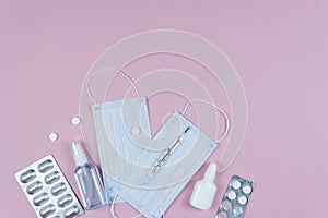 Protective medicine mask, antiseptic thermometer and pills on pink background, flat lay. Concept of doctor table and health care