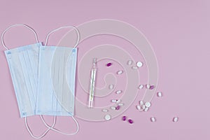 Protective medicine mask, thermometer and pills on pink background, flat lay. Concept of doctor table and health care