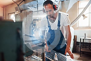 In protective noiseless headphone. Man in uniform works on the production. Industrial modern technology