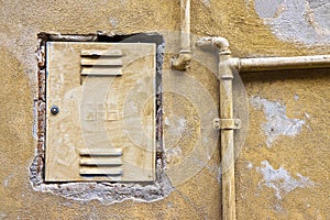 Protective old metal box of methane gas meter against a damaged plaster wall with metal pipeline