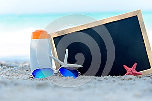 Protective sunscreen or sunblock and sunbath lotion in white plastic bottles with sandals on tropical beach.  Closeup of a chalkbo