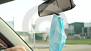 A protective surgical face mask hangs on the rearview mirror while driving.