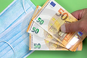 Surgical mask with several 50 euro notes held by a man\`s hand to illustrate the skyrocketing prices due to out of stoc