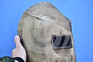 Protective welding shield in hand on a blue background